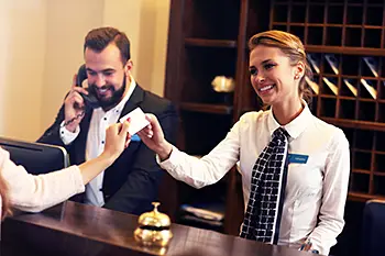 Smiling hotel receptionist handing over a RFID card to a happy hotel guest. Hotell using high-quality digitalized logistics systems from acg pulse